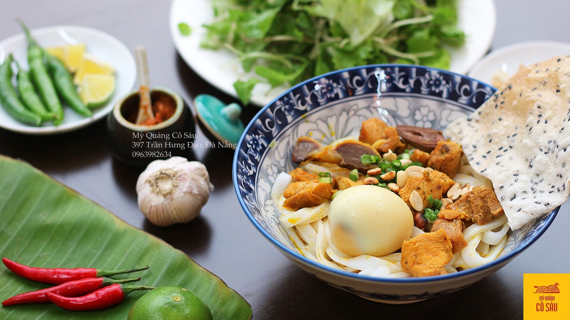 Quán mì Quảng cô Sáu tọa lạc ngay sát khu phố cổ sầm uất, nổi tiếng với mức giá bình dân và hương vị truyền thống khó quên. Một tô mì đầy đặn với sợi mì dai mềm, topping đầy đủ từ tôm, thịt đến trứng, đi kèm rau sống tươi xanh được bày trí hấp dẫn. Điểm đặc biệt làm nên tên tuổi quán là chén nước mắm pha cay nhẹ, thơm nồng, ăn kèm mì Quảng thì “chuẩn bài”. Với thâm niên mấy chục năm phục vụ thực khách gần xa, quán cô Sáu lúc nào cũng đông nghịt, thế nên hãy kiên nhẫn một chút để thưởng thức trọn vẹn hương vị mì Quảng đậm đà, đúng điệu.