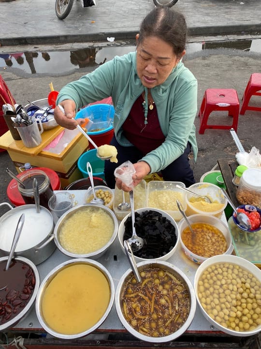 Chè cô Hai là một trong những quán chè vỉa hè ngon nức tiếng tại Hội An, nơi bạn có thể vừa nghỉ chân vừa thưởng thức hương vị ngọt mát giữa lòng phố cổ. Sau khi dạo quanh những con phố vàng ruộm màu thời gian, đừng quên ghé lại quán để nếm thử các món chè dân dã như tào phớ, chè bắp, chè đậu ván, chè đậu đen, chè thập cẩm, chè hạt sen… mỗi loại đều mang đậm hương vị truyền thống, giản dị mà khó quên.