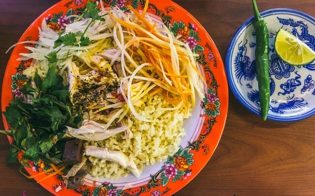 Nếu đã từng một lần thưởng thức cơm gà tại quán, hẳn bạn sẽ khó quên được hương vị đặc trưng nơi đây. Cơm được nấu vô cùng công phu: chọn loại gạo tám dẻo, kết hợp cùng nước luộc gà và lá dừa tạo nên vị thơm béo, đậm đà lan tỏa ngay từ miếng đầu tiên. Hạt cơm bóng bẩy, mềm dẻo nhưng không hề nhão – đủ khiến bất kỳ ai cũng phải gật gù tán thưởng.