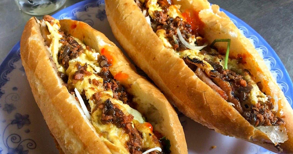 Nằm trong danh sách những địa chỉ ăn vặt Hội An không thể bỏ qua, Bánh mì Madam Khánh đã hơn 30 năm gìn giữ hồn cốt ẩm thực phố cổ. Không cầu kỳ trong menu với chỉ 5 món, nhưng mỗi chiếc bánh ở đây đều là sự hòa quyện tinh tế giữa lớp vỏ giòn rụm và nhân đậm đà – từ bánh mì thập cẩm đủ đầy, bánh mì heo mềm thơm, đến bánh mì gà đậm vị hay miếng thịt nướng ám khói. Mỗi loại nhân mang một cá tính riêng, nhưng tất cả đều cùng chung tiêu chuẩn: ngon khó cưỡng.
