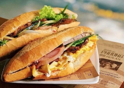 Bánh mì Phượng là tiệm bánh mì trứ danh tại Hội An, từng được đưa lên bản đồ ẩm thực thế giới khi đầu bếp kiêm MC huyền thoại Anthony Bourdain ghé thăm và dành lời khen ngợi vào năm 2009. Đây là một trong những địa chỉ ăn vặt Hội An nổi tiếng bậc nhất phố cổ với thực đơn phong phú, quy tụ hàng chục loại nhân hấp dẫn như chả, lạp xưởng, pate, xúc xích, jambon, thịt xông khói... Mỗi ổ bánh mì được kết hợp hài hòa giữa lớp nhân đầy đặn, rau thơm, dưa chua và đặc biệt là nước sốt cùng mayonnaise độc quyền, tạo nên hương vị đậm đà khó quên.