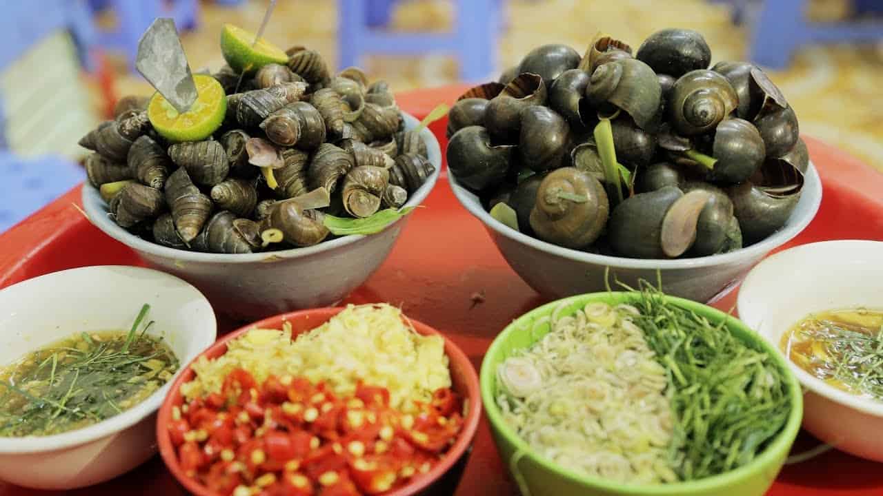 Ốc Trộn Cô Hà là một trong những điểm hẹn ăn vặt quen thuộc của giới trẻ Hội An. Nổi bật với món ốc trộn đậm đà, quán còn ghi điểm nhờ thực đơn phong phú, hấp dẫn như bò rim thơm lừng, bánh tráng kẹp giòn rụm, bánh tráng trộn đậm vị và nem nướng béo ngậy. Đây chắc chắn là địa chỉ lý tưởng cho những ai muốn khám phá ẩm thực đường phố Hội An.